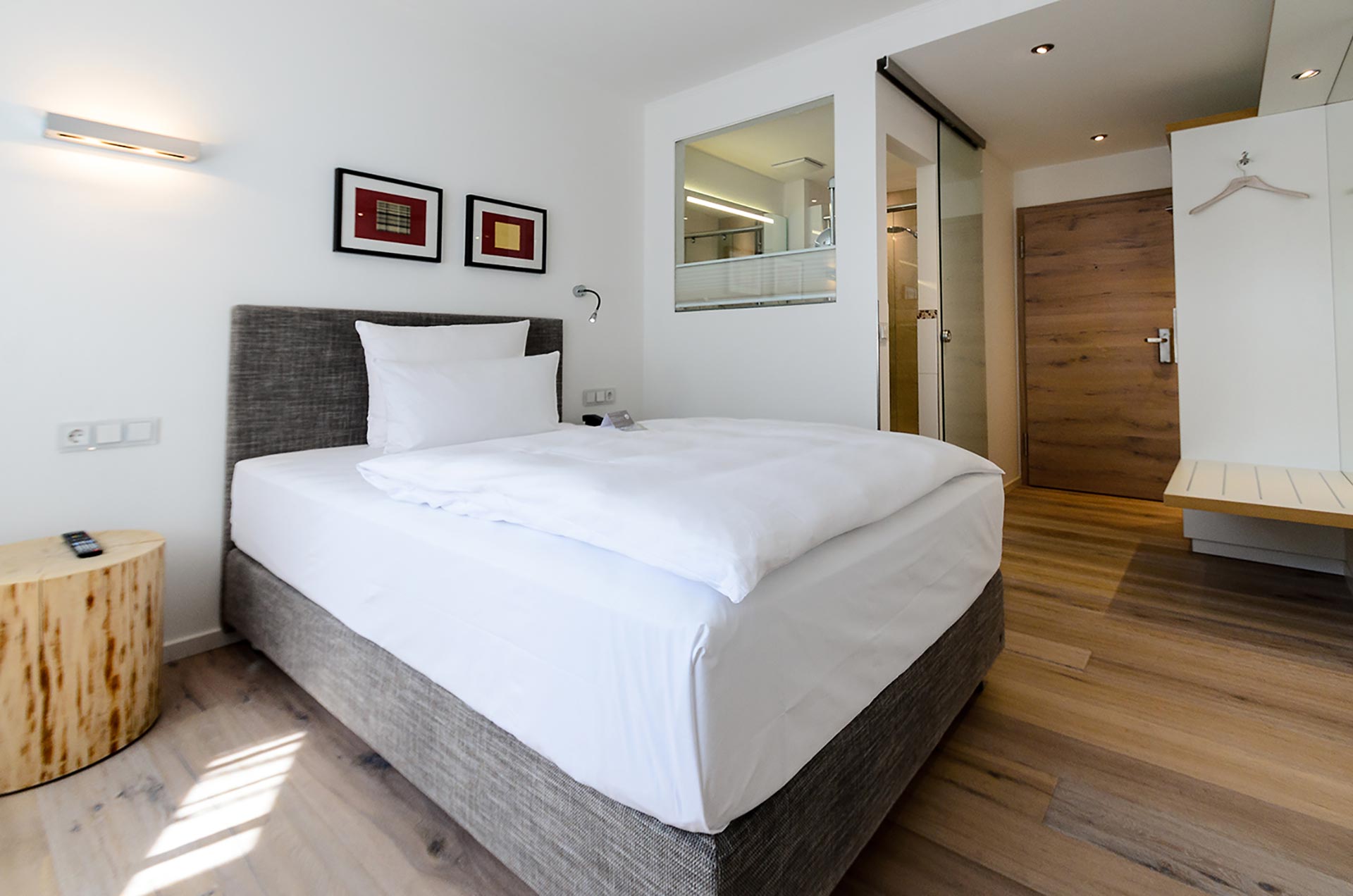 Das Bild zeigt ein modernes und ansprechend gestaltetes Hotelzimmer im Hotel Schwanen in Metzingen. Der Raum ist hell und freundlich, mit einem komfortablen Bett, das mit frischen, weißen Bettwaren ausgestattet ist. Die gemütliche Atmosphäre wird durch die stilvolle Einrichtung und die hellen Holzböden unterstrichen.