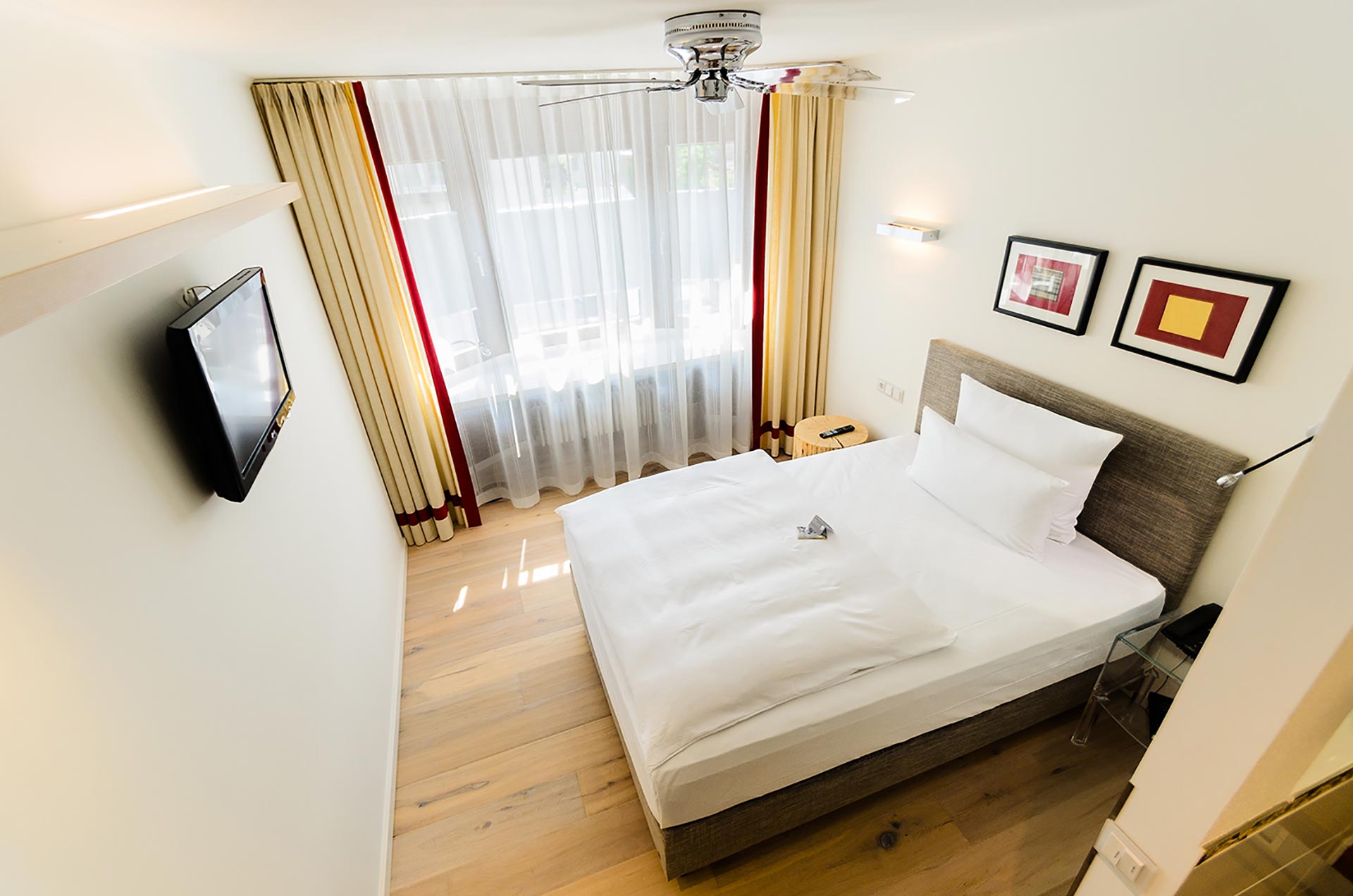 Das Bild zeigt ein modernes und stilvolles Zimmer im Hotel Schwanen in Metzingen. Der Raum ist hell und freundlich gestaltet, mit großen Fenstern, die viel Tageslicht hereinlassen. Die sanften Farbnuancen und die geschmackvolle Einrichtung schaffen eine angenehme Atmosphäre, ideal für einen erholsamen Aufenthalt.